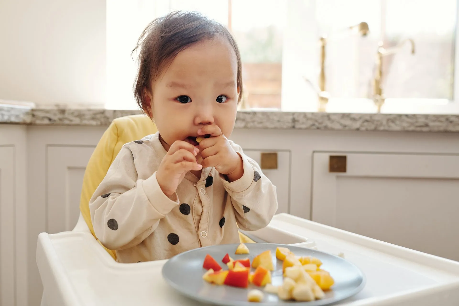 Toddler happily eating fruit in a high chair at home